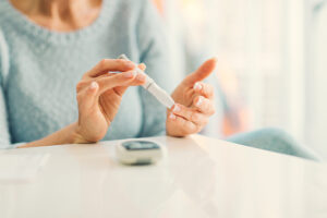 Mature woman doing blood sugar test at home in a living room. Selective focus to her finger.